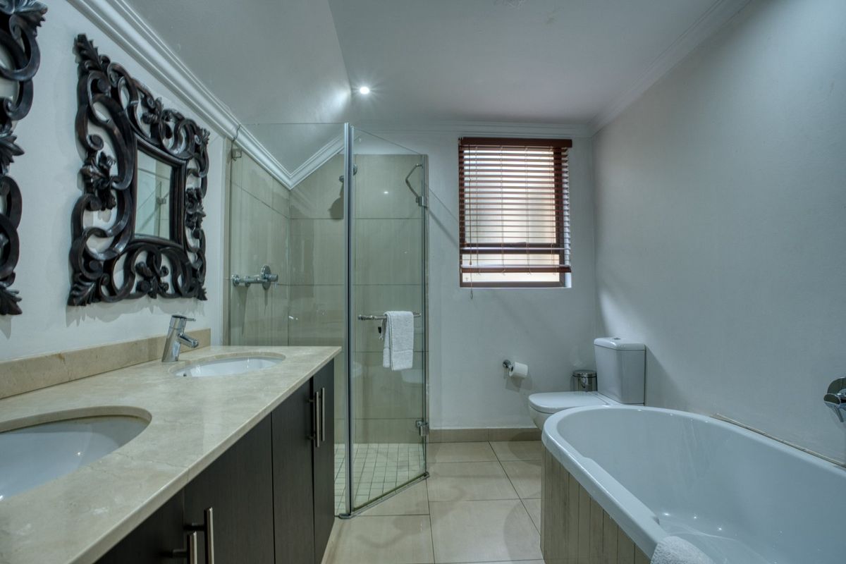 Modern bathroom featuring a double vanity with stone countertop, glass-enclosed shower, and a freestanding bathtub.
