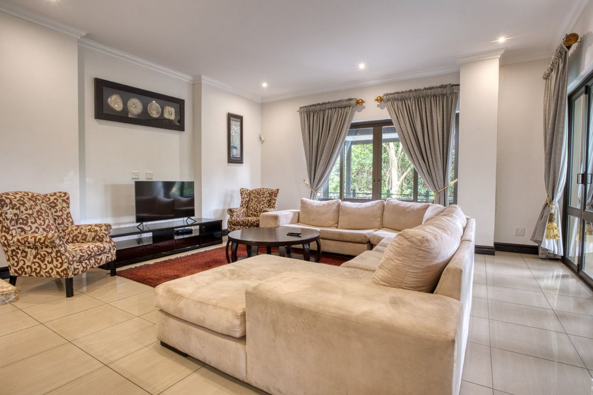 Spacious living room featuring neutral floor tiles, recessed downlighting, and large glass sliding doors providing natural light and garden access.