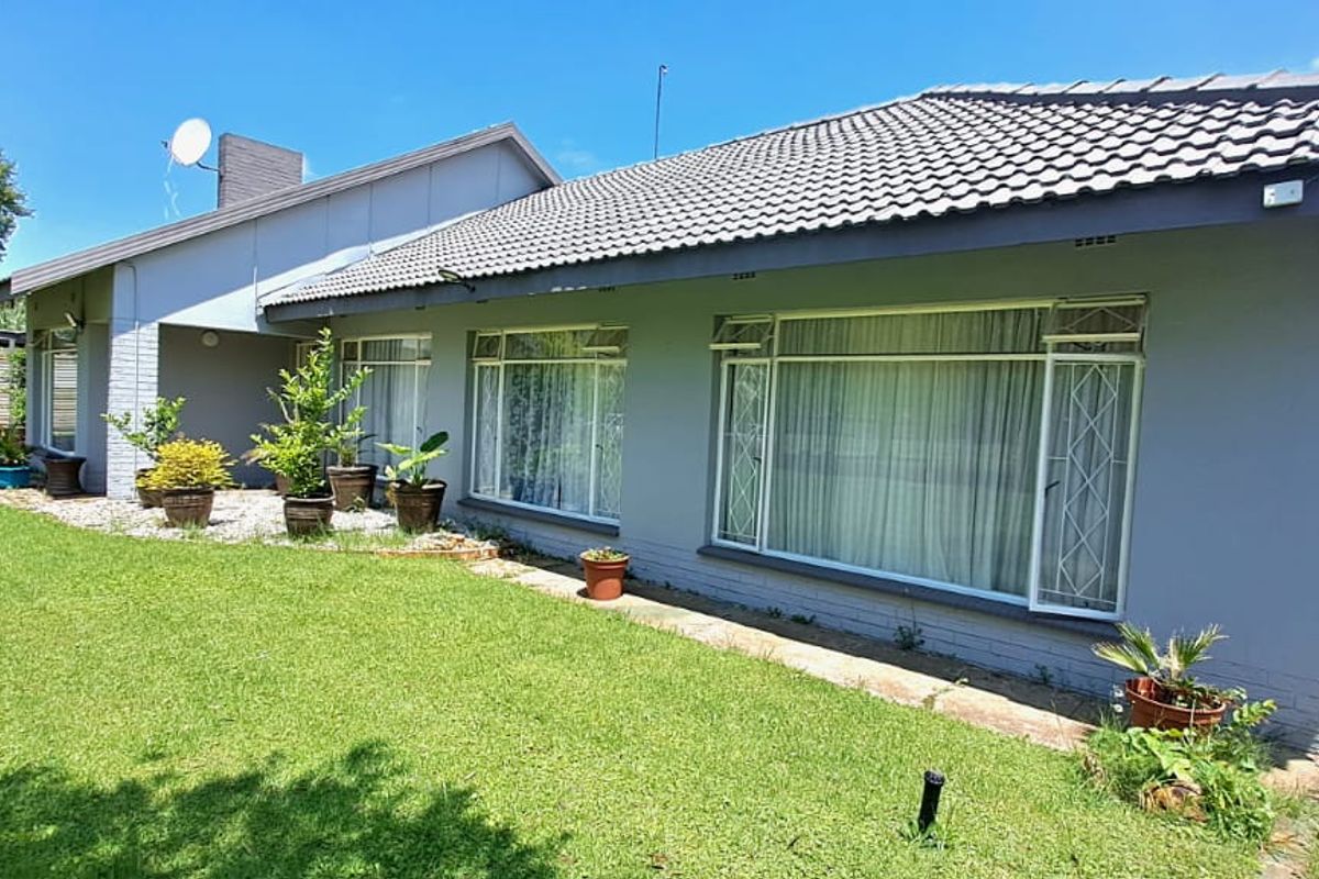 A view of the rear exterior of the house, featuring a tiled roof, large windows with security bars, and a well-maintained lawn.