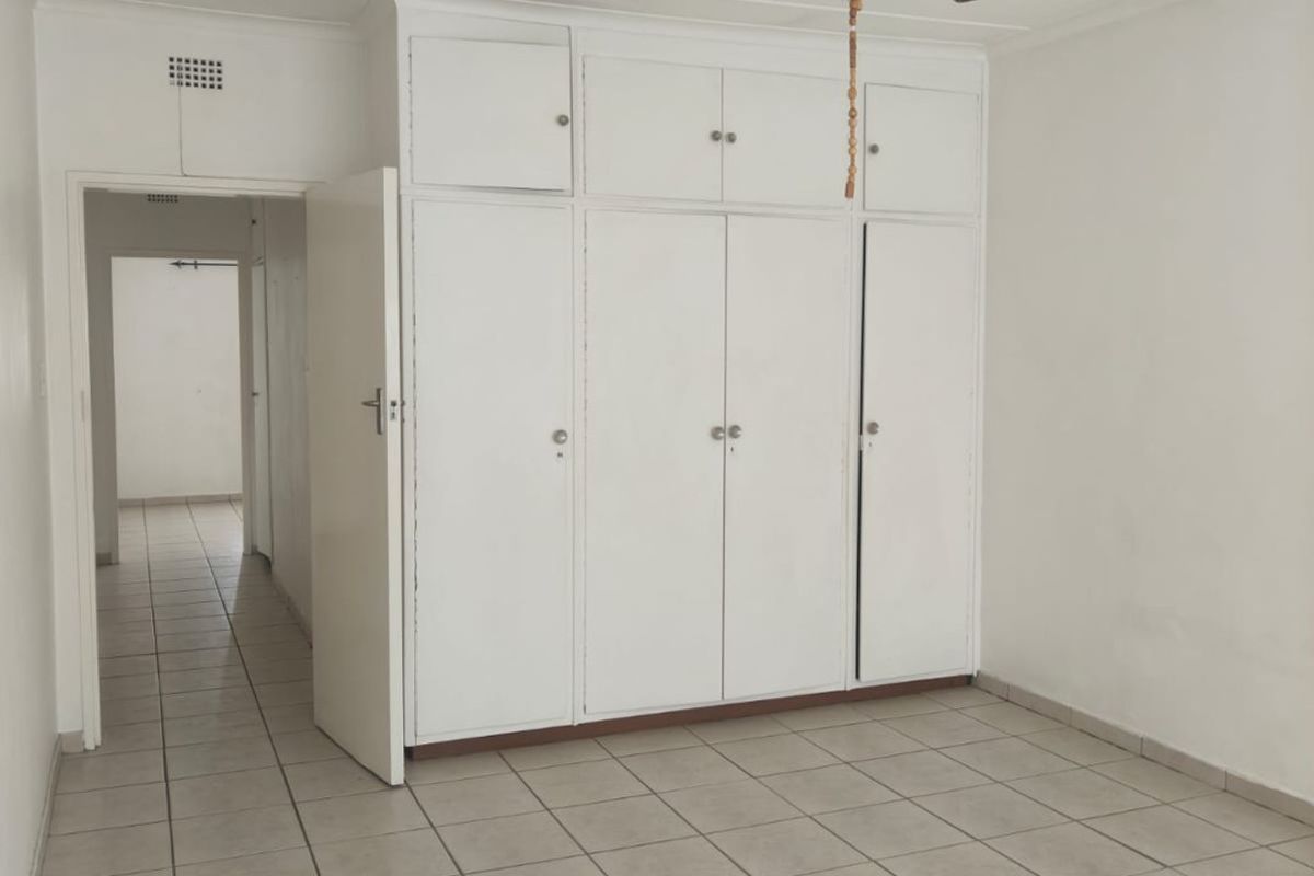 A bedroom featuring built-in floor-to-ceiling cupboards, tiled flooring, and a ceiling fan, offering a functional and neutral living space.