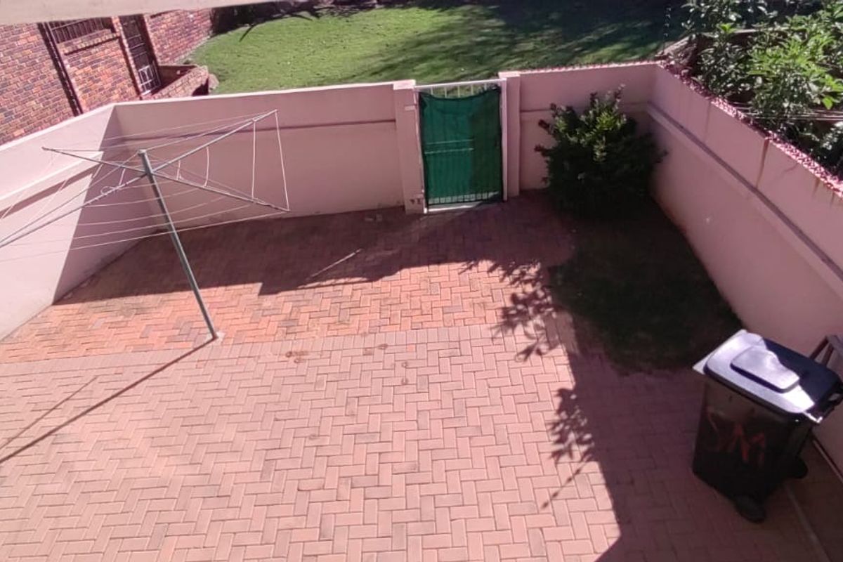 A private rear courtyard featuring paved flooring, a perimeter wall, and a metal gate, providing a functional outdoor space.