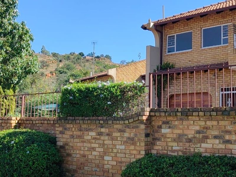 Front view of a double-story face brick townhouse featuring a secure boundary wall, metal fencing, and an upper-level balcony.