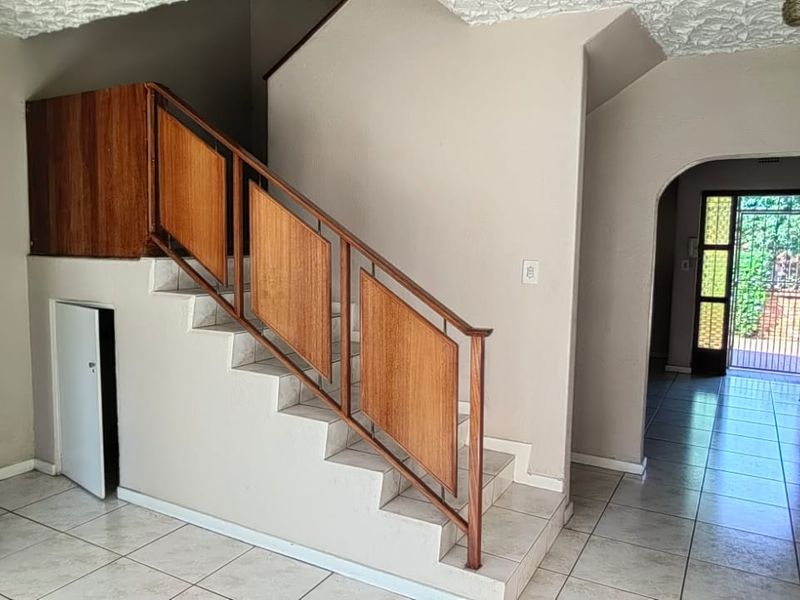 Entrance area featuring a staircase with a wooden balustrade, tiled flooring, and an arched doorway leading to the exterior security gate.