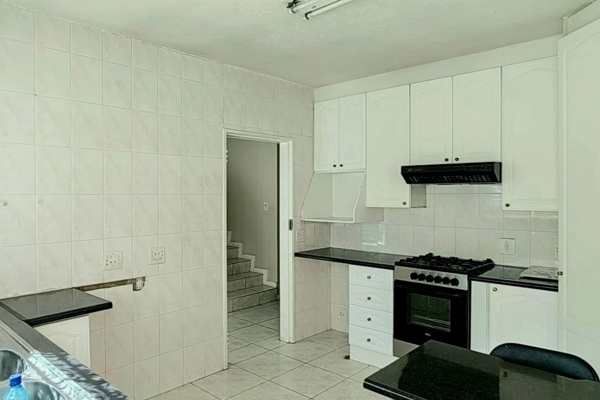 A functional kitchen featuring white cabinetry, granite countertops, a gas stove with extractor fan, and tiled flooring, offering a clean and practical workspace.