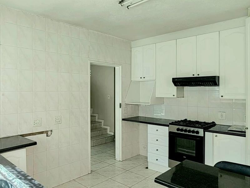 A functional kitchen featuring white cabinetry, granite countertops, a gas stove with extractor fan, and tiled flooring, offering a clean and practical workspace.