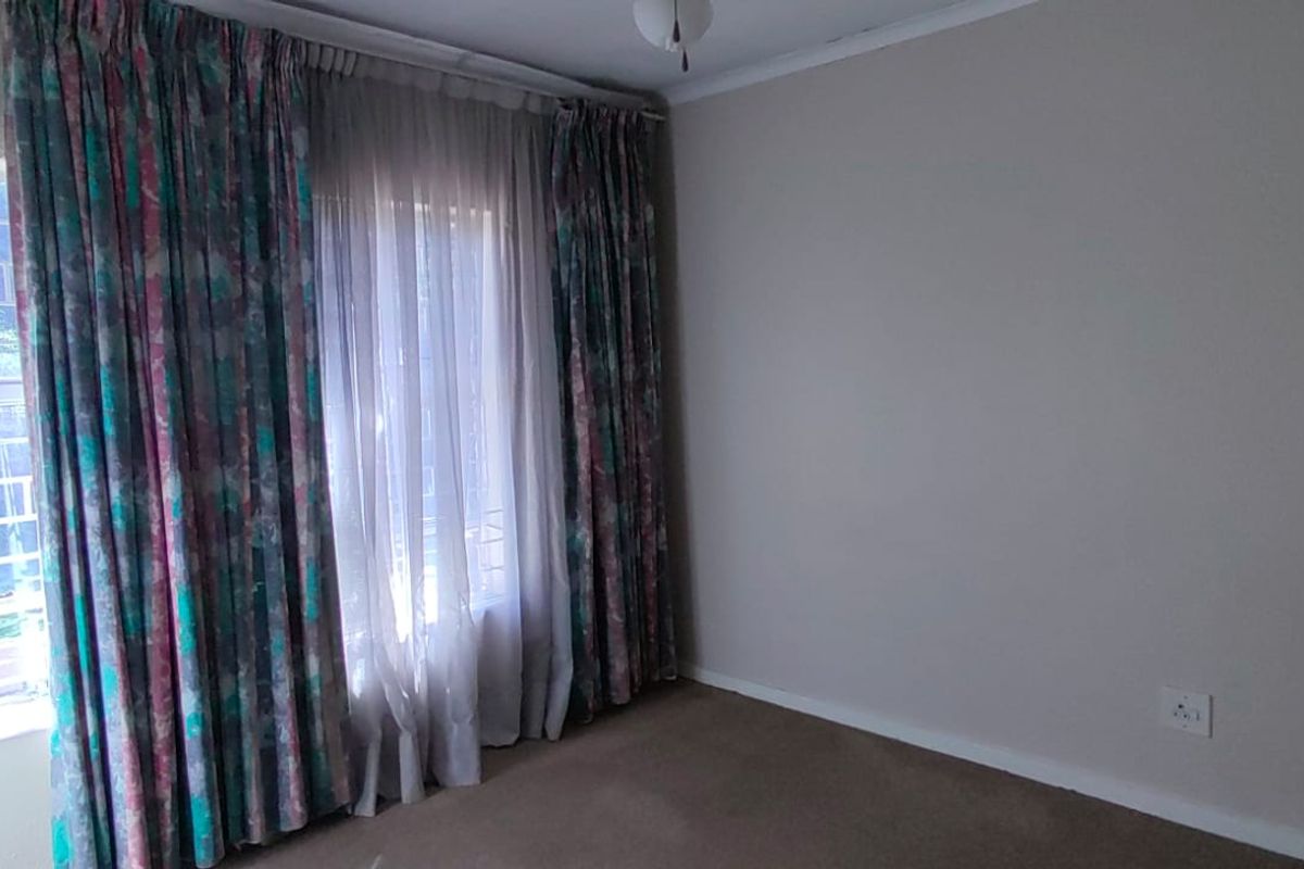 A vacant bedroom featuring neutral wall paint, carpeted flooring, and large windows with existing curtain tracks.