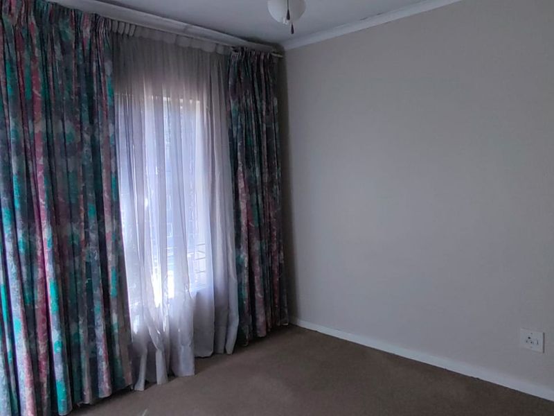 A vacant bedroom featuring neutral wall paint, carpeted flooring, and large windows with existing curtain tracks.