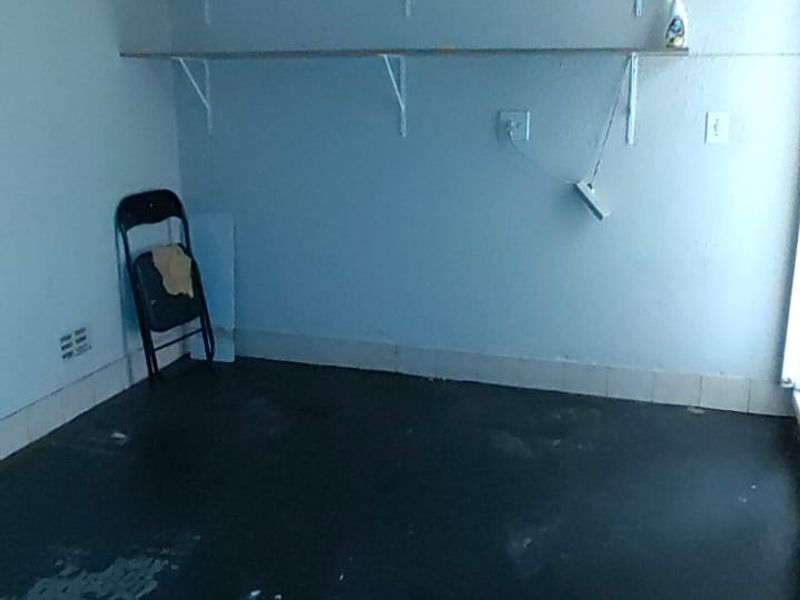 A vacant utility or storage space featuring wall-mounted shelving and electrical points, requiring floor and wall refinishing.