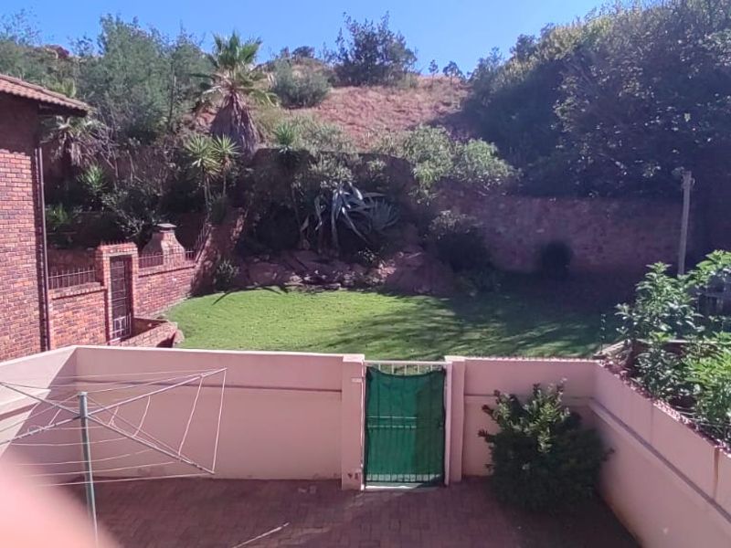 A rear view of the townhouse featuring a paved patio area, a private garden, and brick exterior walls.