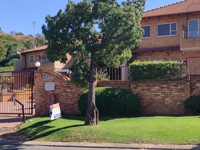 Front elevation of a brick townhouse complex featuring a secure gated entrance, paved driveway, and established garden area.
