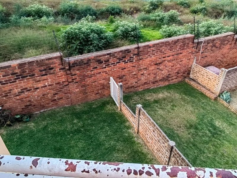 An elevated view of a private rear garden featuring a lawn, brick boundary walls with electric fencing, and a weathered metal balcony railing.