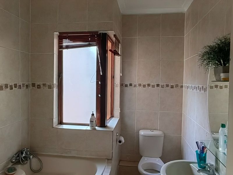 A functional bathroom featuring tiled walls, a bathtub, a pedestal basin, and a toilet, with a window providing natural light.