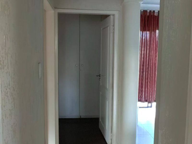 A tiled hallway featuring a structural column, built-in storage cupboards, and decorative ceiling molding, leading into an adjacent room.