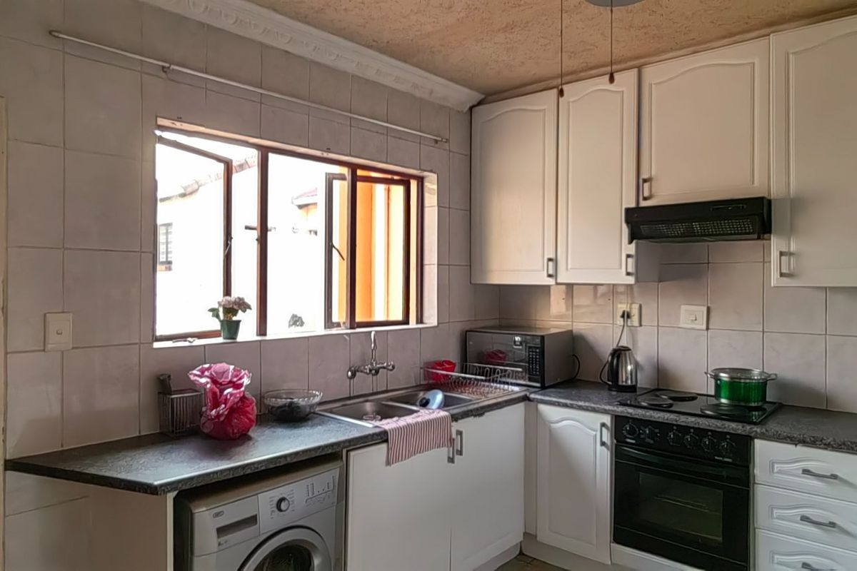 Functional kitchen featuring white cabinetry, laminate countertops, built-in oven with hob, extractor fan, and tiled splashback with space for under-counter appliances.