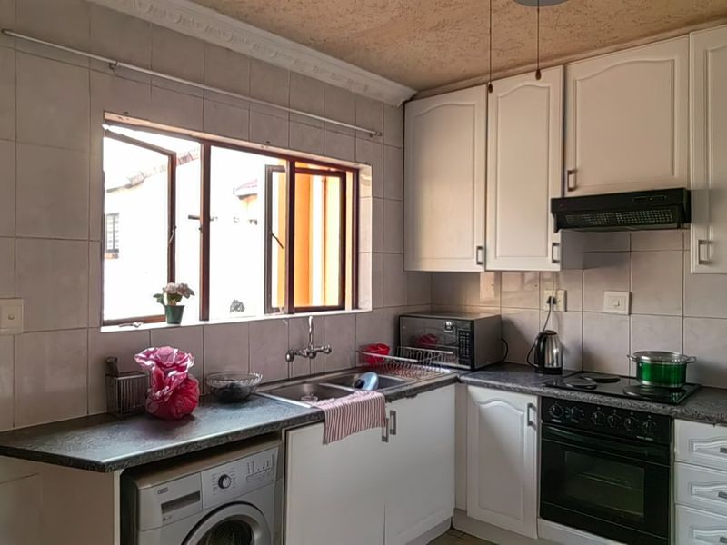 Functional kitchen featuring white cabinetry, laminate countertops, built-in oven with hob, extractor fan, and tiled splashback with space for under-counter appliances.