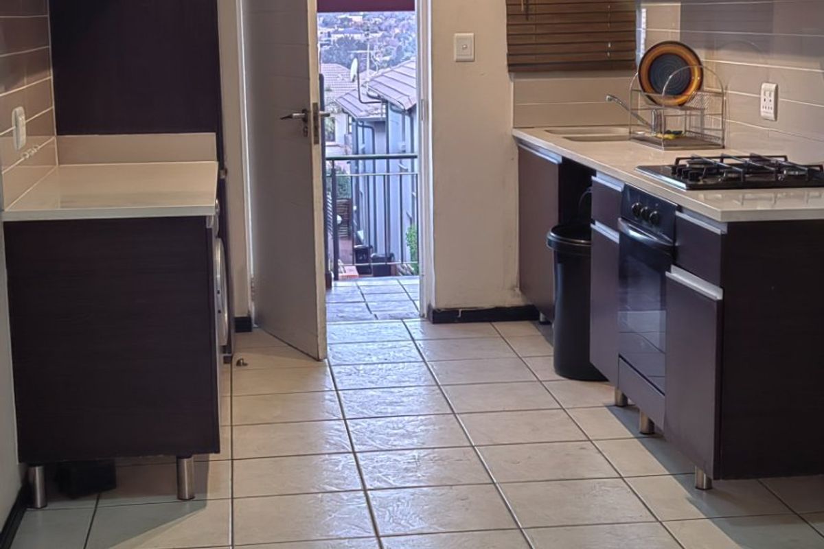 Functional kitchen featuring dark wood cabinetry, light stone countertops, gas hob, built-in oven, and direct access to a balcony.