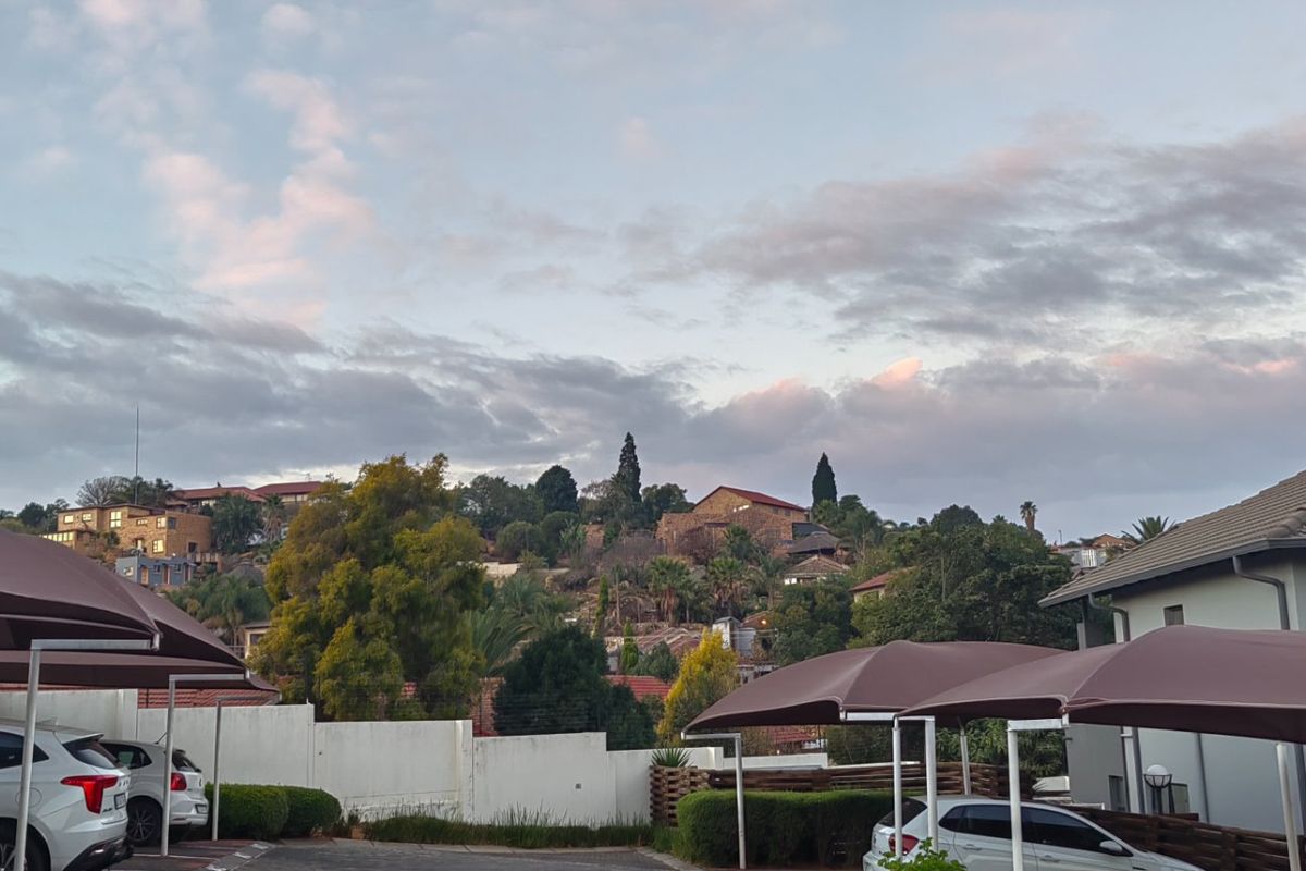 Exterior view of the apartment complex grounds featuring covered parking bays and perimeter walling against a scenic hillside backdrop.