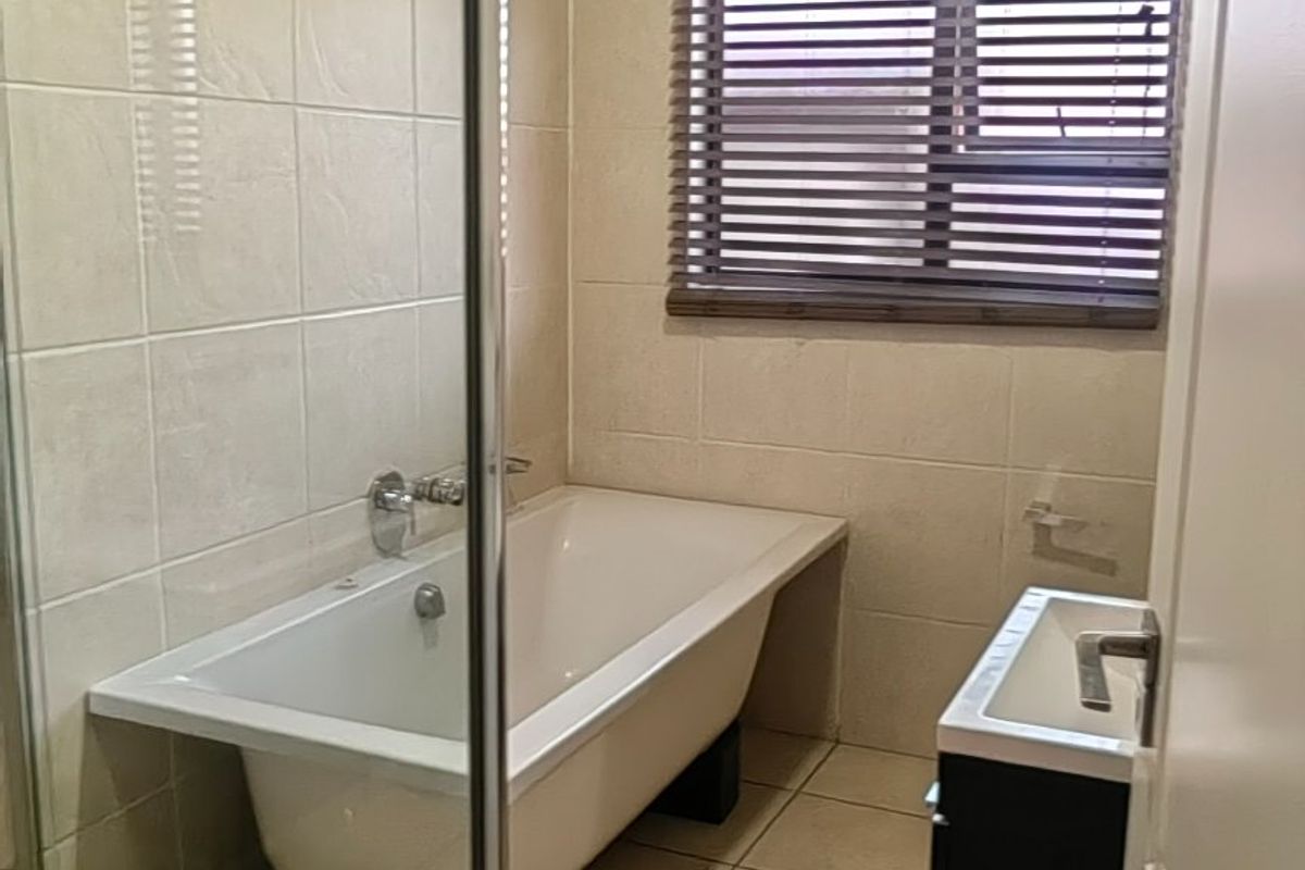 A functional bathroom featuring a glass shower enclosure, a freestanding bathtub, and a wall-mounted vanity with neutral floor-to-ceiling tiling.