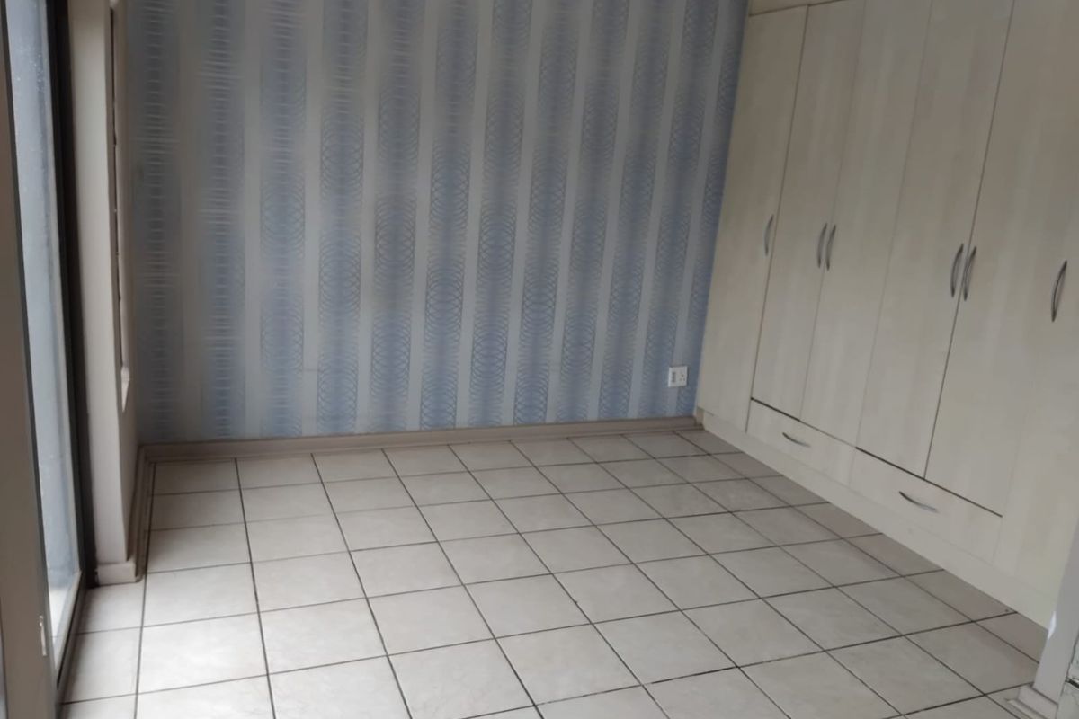 A bright, empty bedroom featuring tiled flooring, built-in cupboards, and a sliding glass door providing access to the exterior.