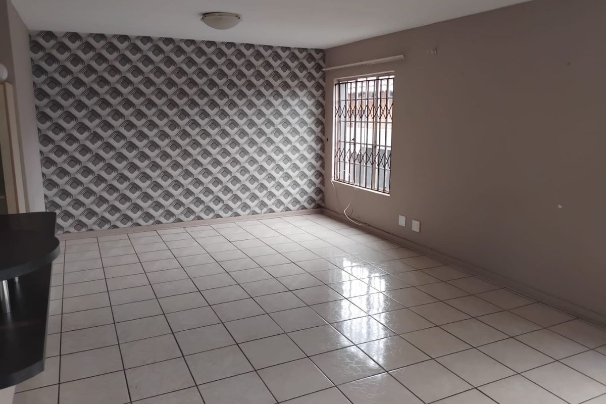 An empty living room featuring tiled flooring, a security gate on the window, and a patterned feature wall.
