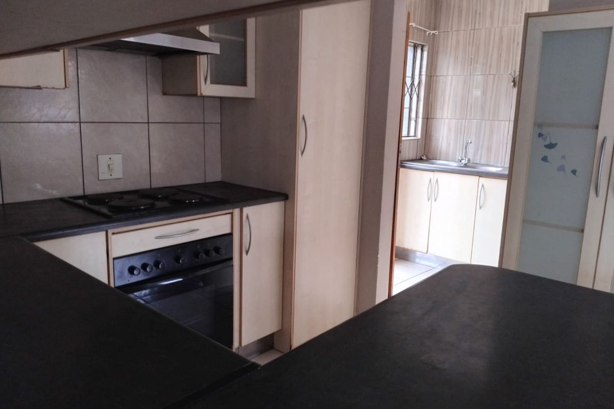 A functional kitchen featuring built-in oven, electric hob, extractor fan, and laminate cabinetry, with an adjacent scullery area visible through the doorway.