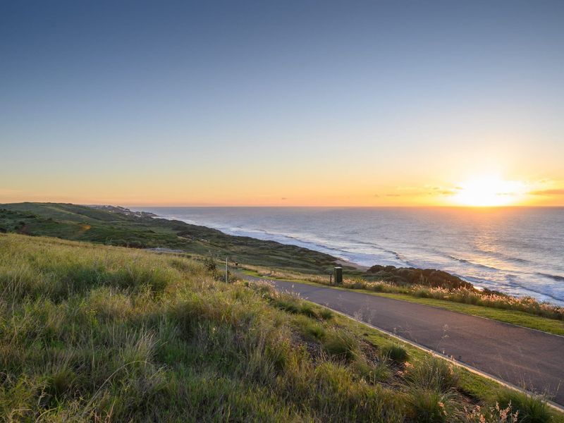 A scenic view of the coastline and ocean at sunset, featuring a paved road winding through the natural landscape.