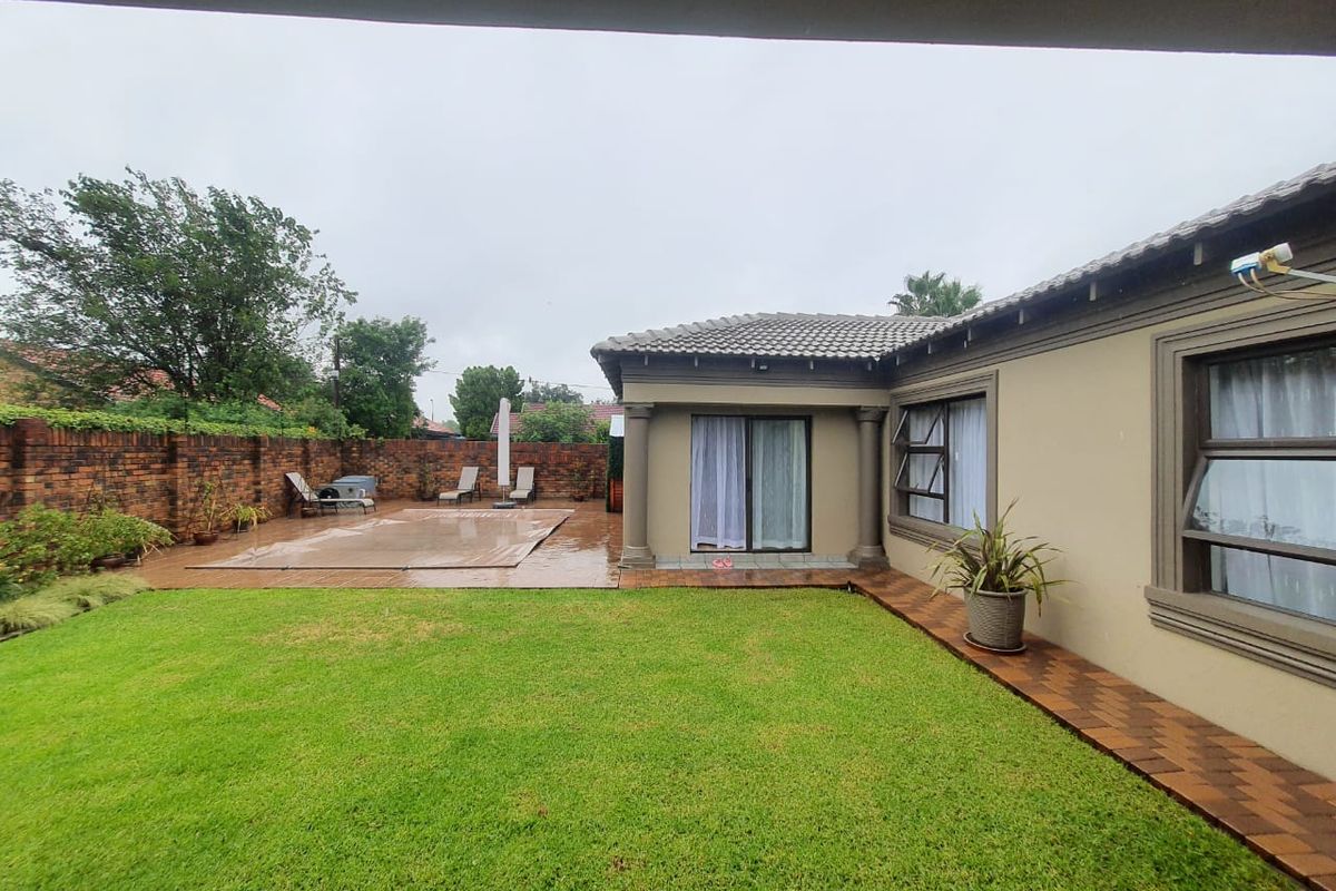 A rear garden view featuring a swimming pool with a cover, paved patio area, and a well-maintained lawn adjacent to the house exterior.
