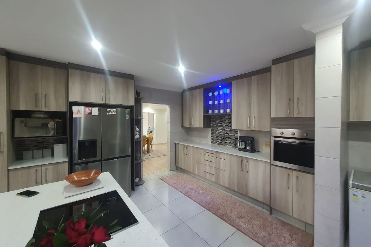 Modern kitchen featuring light wood cabinetry, stone countertops, a central island with a built-in hob, and integrated stainless steel appliances.