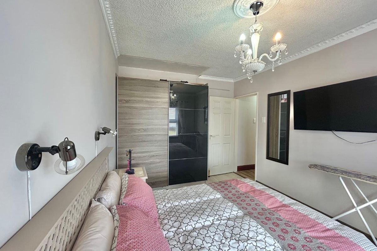 A bedroom featuring built-in wardrobes, decorative ceiling rose with chandelier, wall-mounted reading lights, and a standard door leading to the hallway.