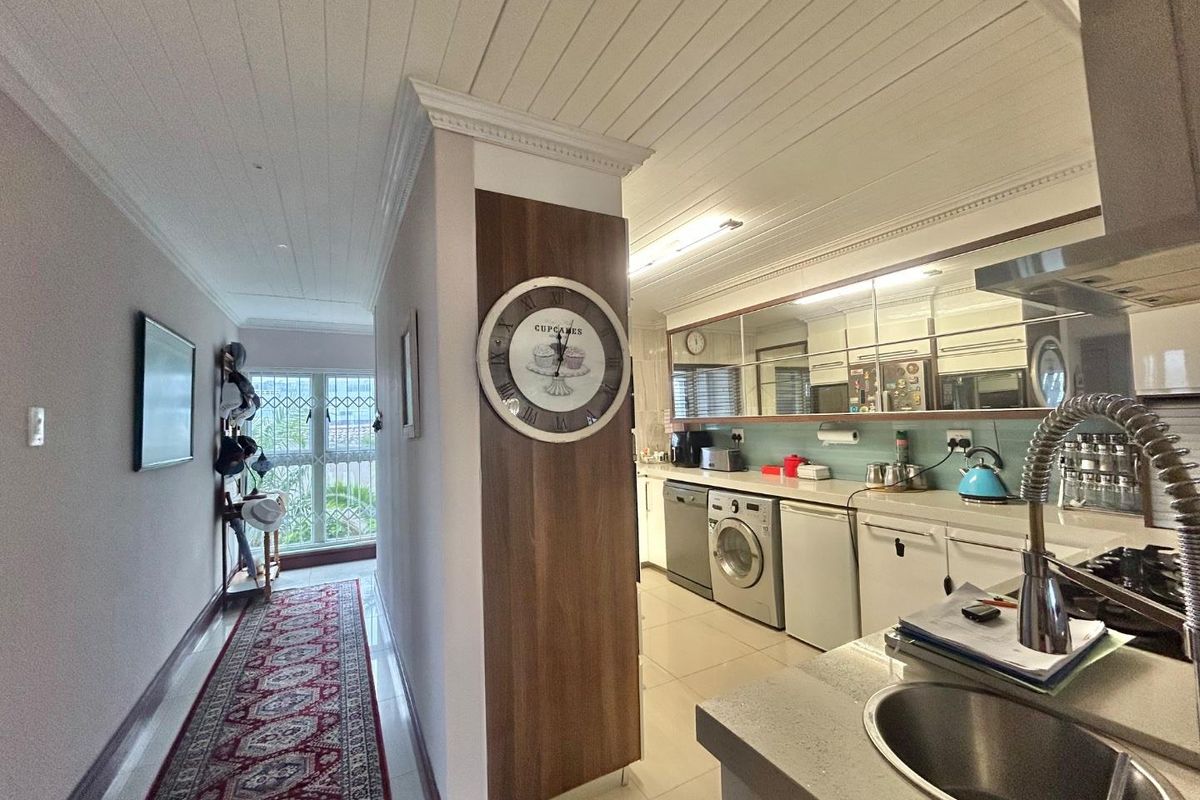 A functional kitchen featuring built-in cabinetry, integrated appliances, and a tiled floor, seamlessly connected to a bright hallway with security gate access.