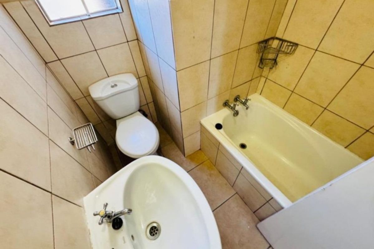 A compact bathroom featuring a standard bathtub, pedestal basin, and toilet with full-height wall tiling and tiled flooring.