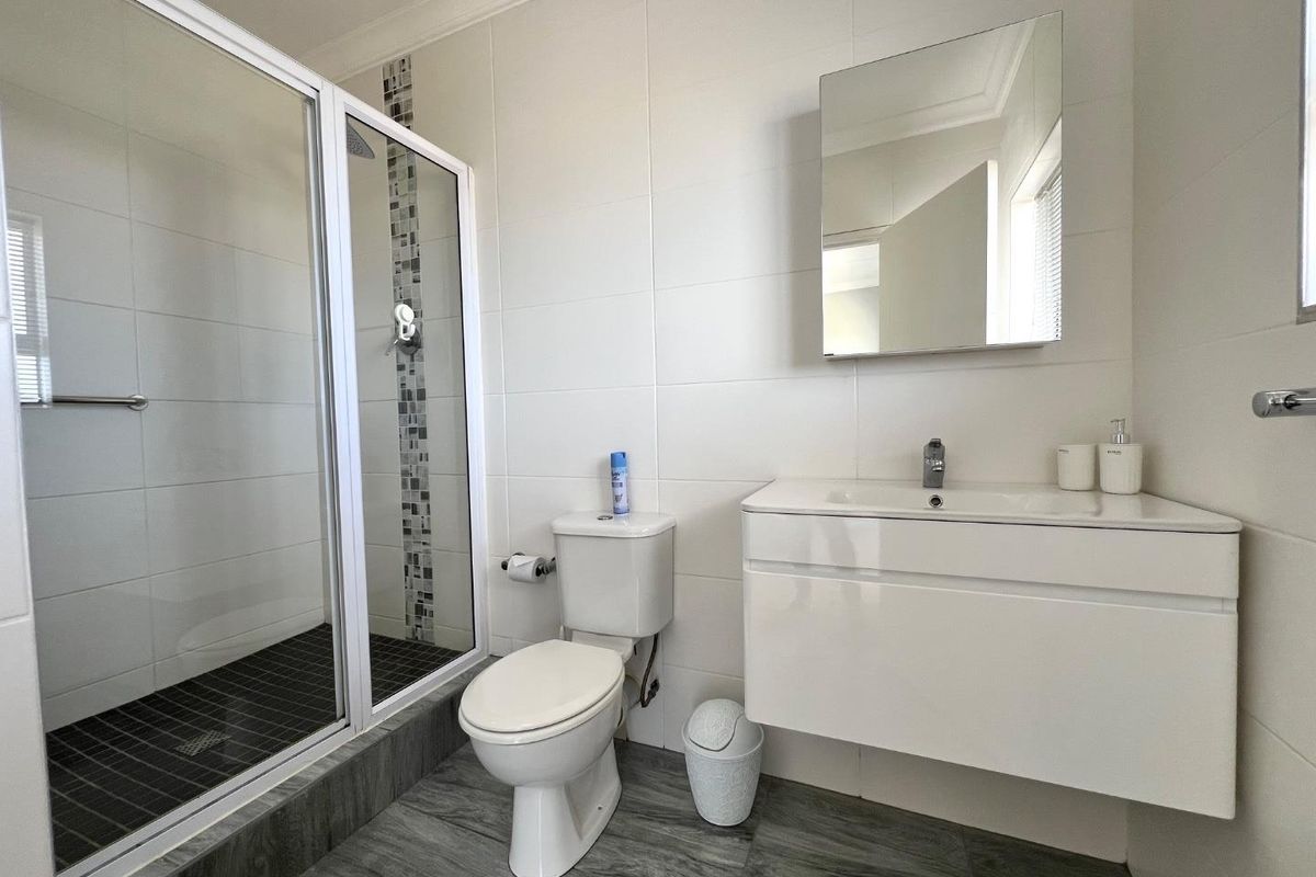 Modern bathroom featuring a glass-enclosed shower, wall-mounted vanity with integrated basin, and contemporary tiled flooring.