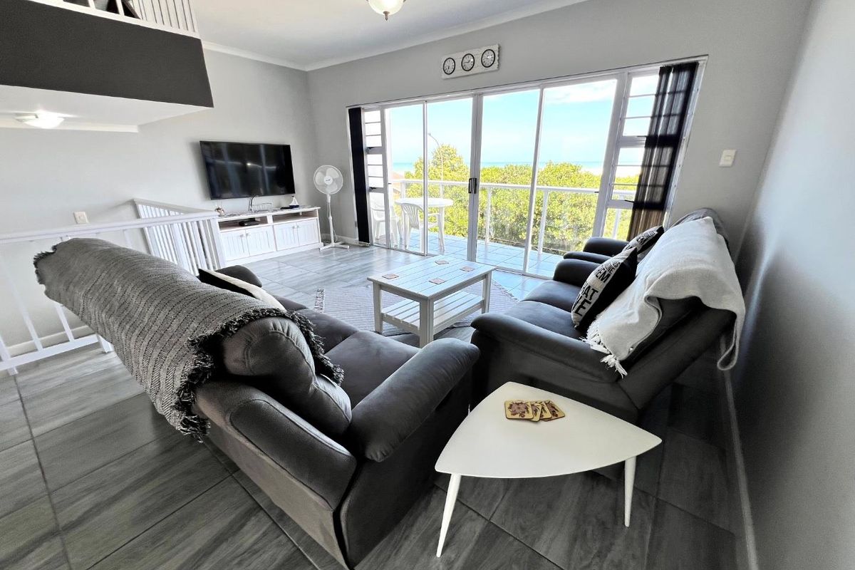 Spacious living area featuring large sliding glass doors that open onto a balcony with scenic views, complemented by modern tiled flooring and staircase access.