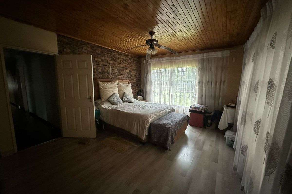 A bedroom featuring a rustic exposed brick feature wall, timber-paneled ceiling, and large windows with natural light.