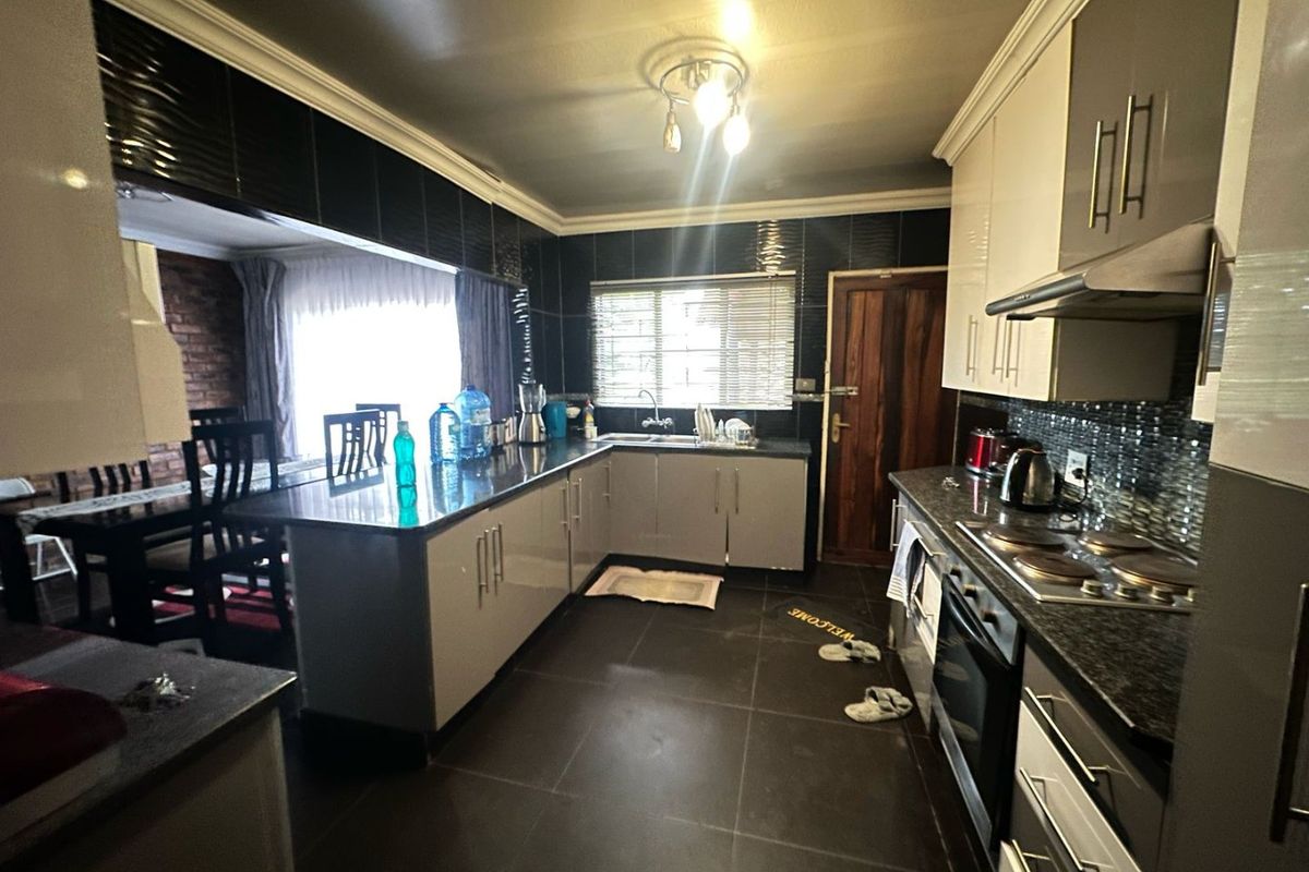 A functional kitchen featuring dark tiled flooring, modern cabinetry, a built-in oven, and a hob with an extractor fan, seamlessly connected to the dining area.