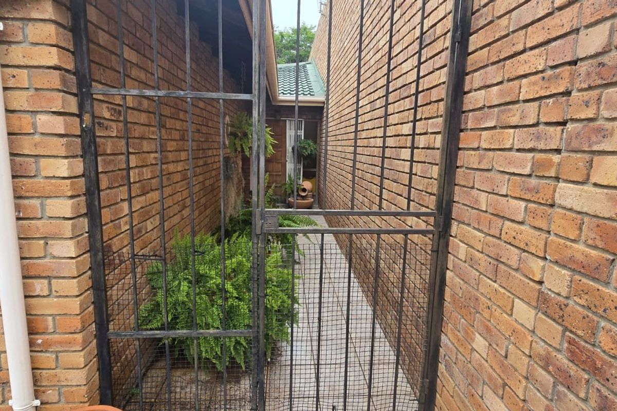 A narrow side passage featuring exposed brick walls, a tiled walkway, and a secure metal gate providing access to the rear of the property.