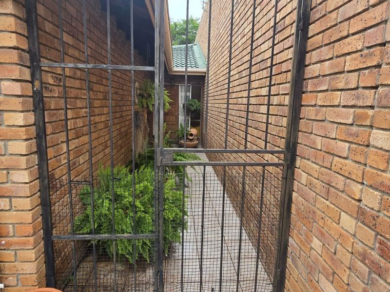 A narrow side passage featuring exposed brick walls, a tiled walkway, and a secure metal gate providing access to the rear of the property.