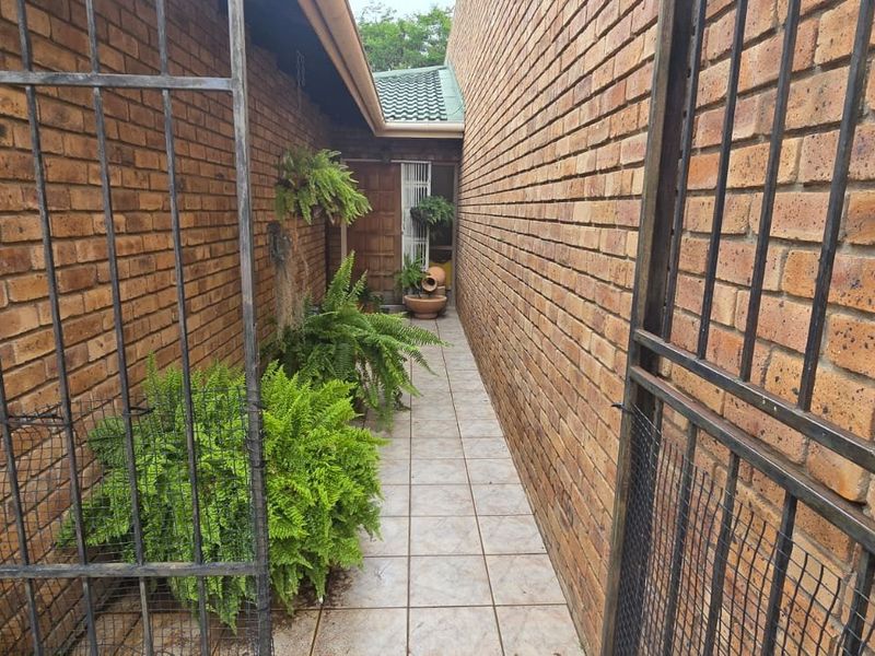 A narrow, tiled side walkway leading to the entrance, enclosed by brick walls and a metal security gate.
