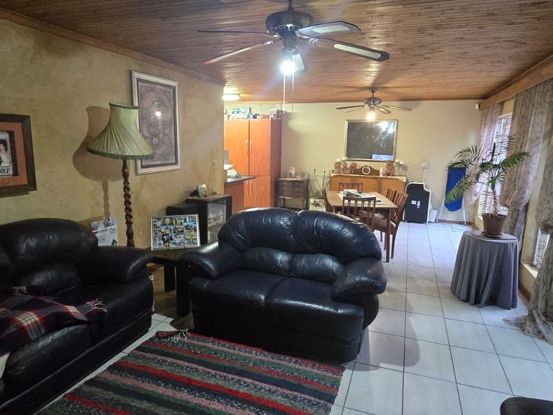 Spacious open-plan living and dining area featuring timber ceilings, ceiling fans, tiled floors, and large sliding glass doors leading to an outdoor patio.