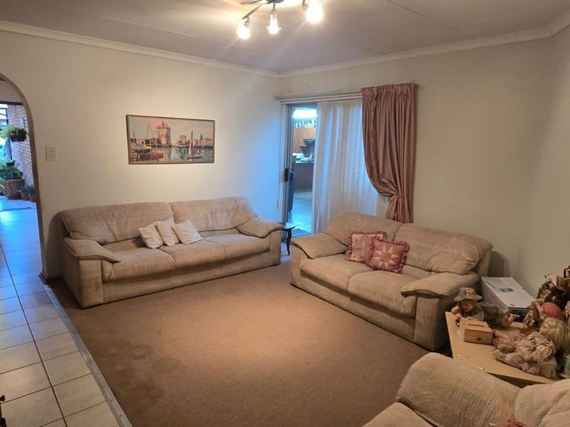 A living room featuring an exposed brick wall, tiled and carpeted flooring, and an archway leading to an adjacent space with sliding door access.