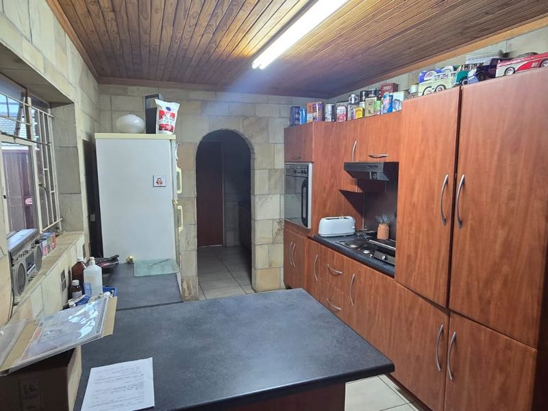A dated kitchen featuring wood-look cabinetry, stone wall cladding, timber ceiling, and built-in appliances, offering significant potential for a modern renovation.
