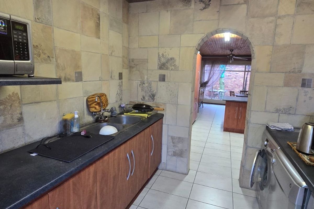 A functional kitchen featuring built-in cabinetry, double sink, and tiled splashbacks, with an arched doorway leading to an adjacent living area.