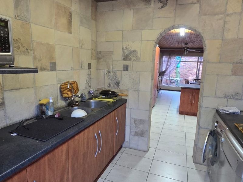 A functional kitchen featuring built-in cabinetry, double sink, and tiled splashbacks, with an arched doorway leading to an adjacent living area.