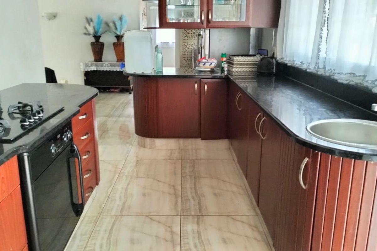 A functional kitchen featuring dark wood cabinetry, granite countertops, a gas hob, built-in oven, and light-toned tiled flooring.