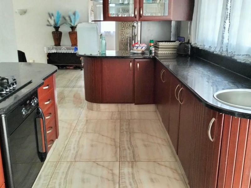 A functional kitchen featuring dark wood cabinetry, granite countertops, a gas hob, built-in oven, and light-toned tiled flooring.