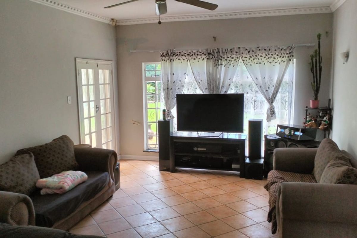 A living room featuring tiled flooring, ceiling fan, and french doors leading to the exterior, with some visible wall surface wear.