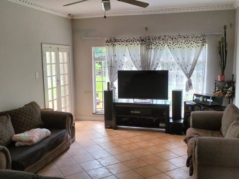 A living room featuring tiled flooring, ceiling fan, and french doors leading to the exterior, with some visible wall surface wear.