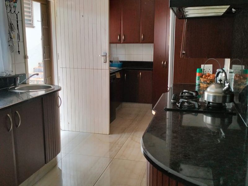 A functional kitchen featuring dark wood cabinetry, granite countertops, a gas hob with extractor fan, and tiled flooring.