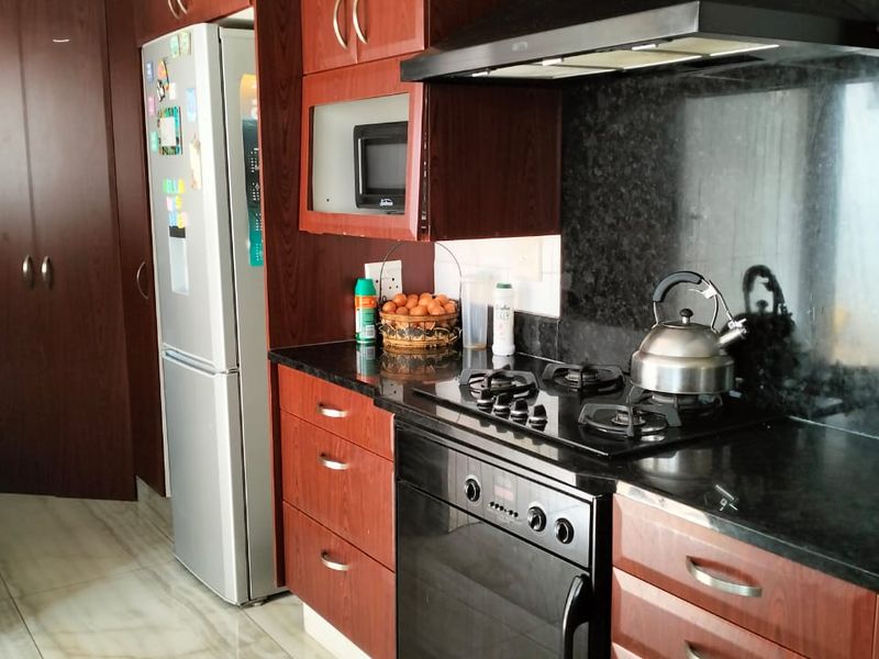 A functional kitchen featuring dark wood cabinetry, granite countertops, a gas hob, built-in oven, and an integrated extractor fan.