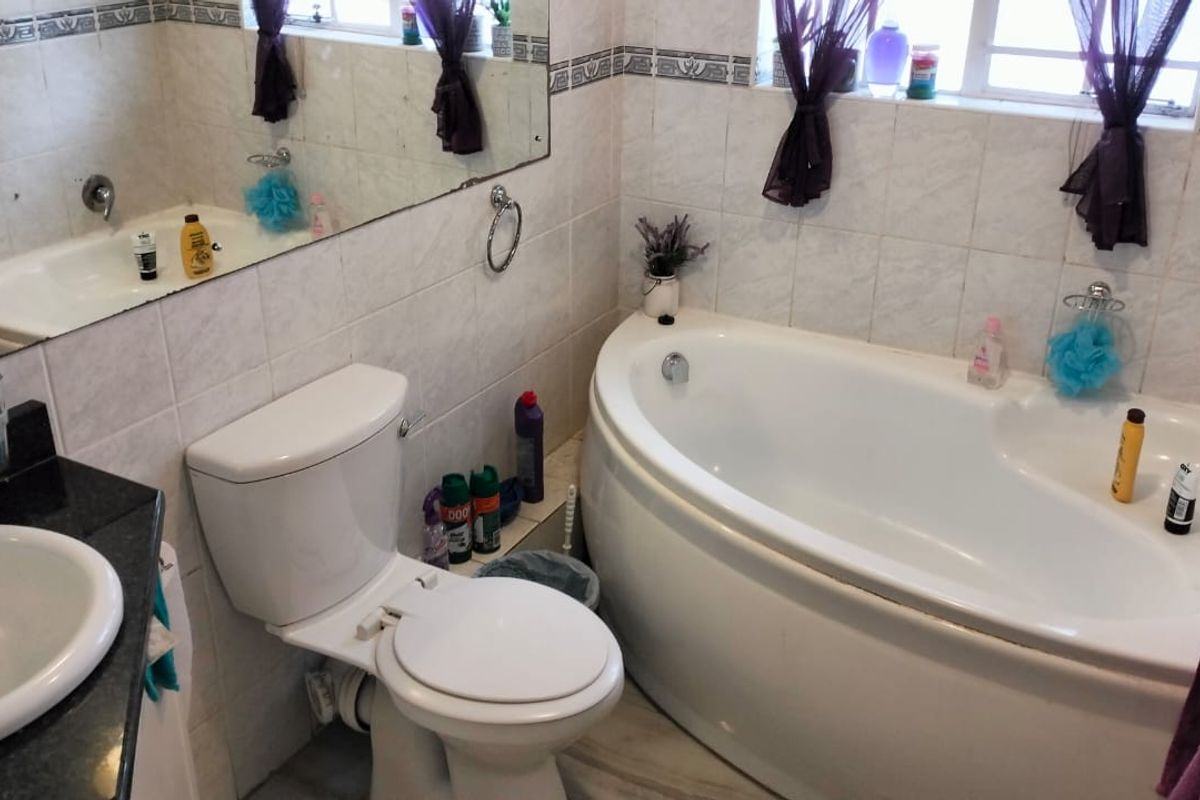 A functional bathroom featuring a corner bathtub, a standard toilet, and a vanity basin with tiled walls and flooring.